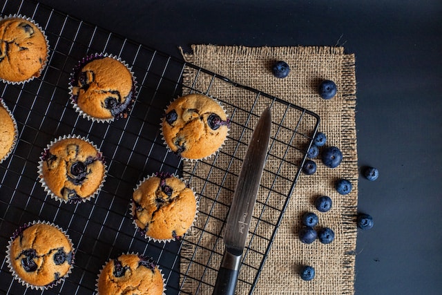 Blueberry muffins on a cooling rack with a knife and pieces of blueberries on the side