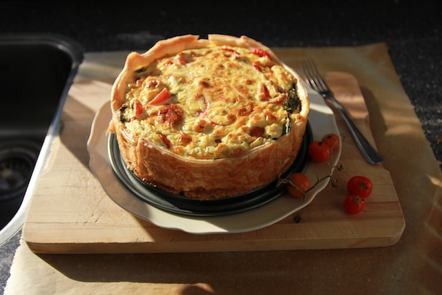 Quiche served on a white plate with cherry tomatoes and a fork on the side