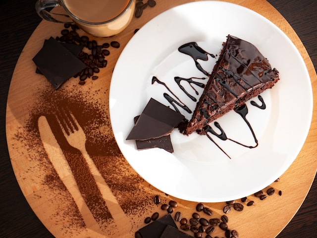 A slice of chocolate cake on a white ceramic plate drizzled with chocolate syrup
