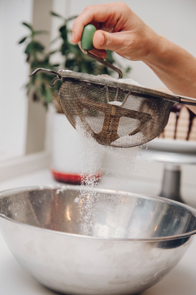 A hand sifting flour onto a mixing bowl