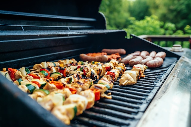Veggies on skewers and sausages cooking on a grill
