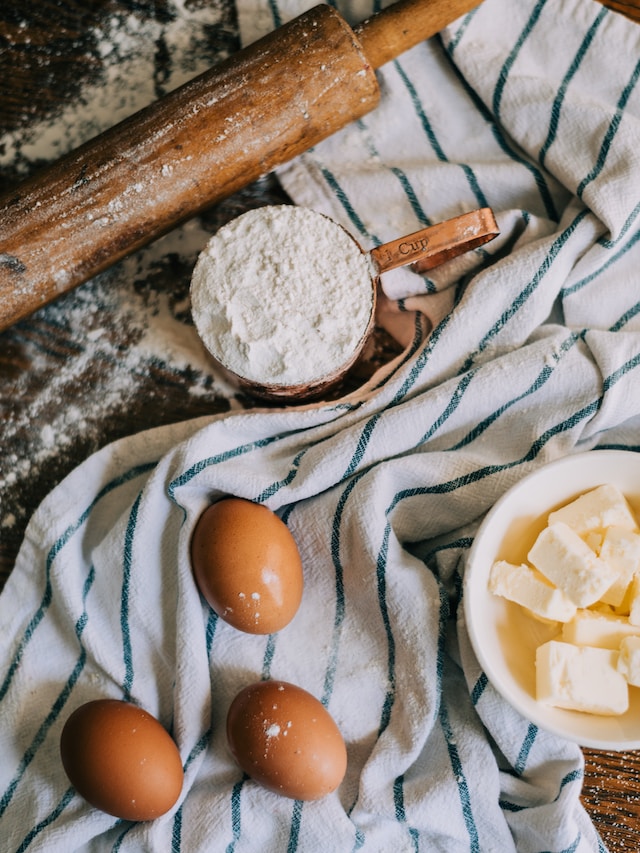 Eggs, butter, flour, and a rolling pin on a table.