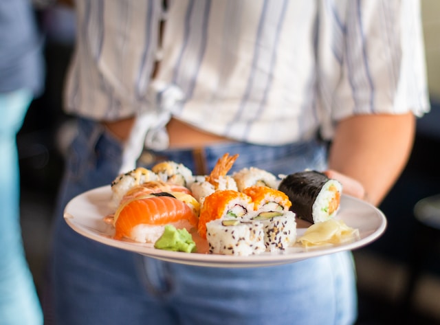 A person holding a plate filled with different types of sushi
