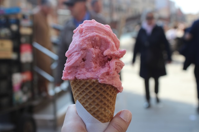 A hand holding a cone filled with pink colored gelato