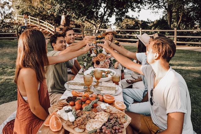 A group of people making a toast over a wooden table laid out with an assortment of food
