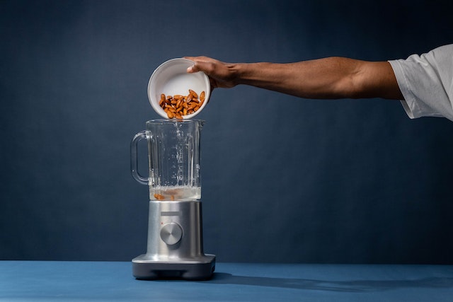 Hand pouring almonds into a blender with water inside