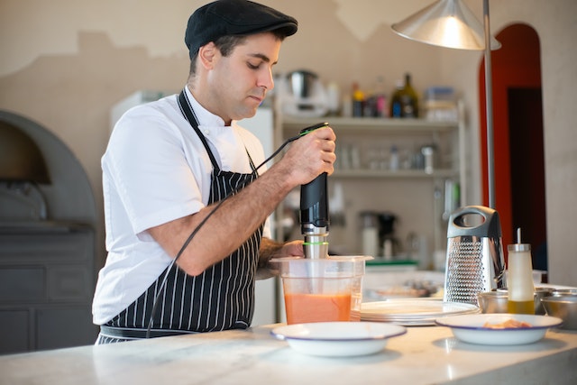 A cook using an immersion blender to make some sauce