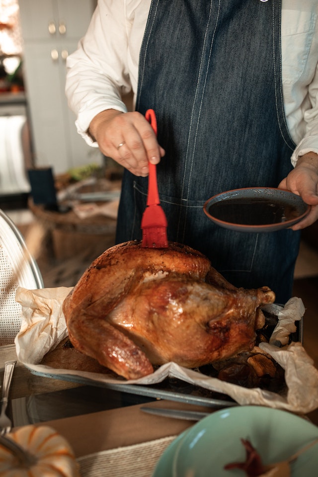 Person basting the chicken using a red brush