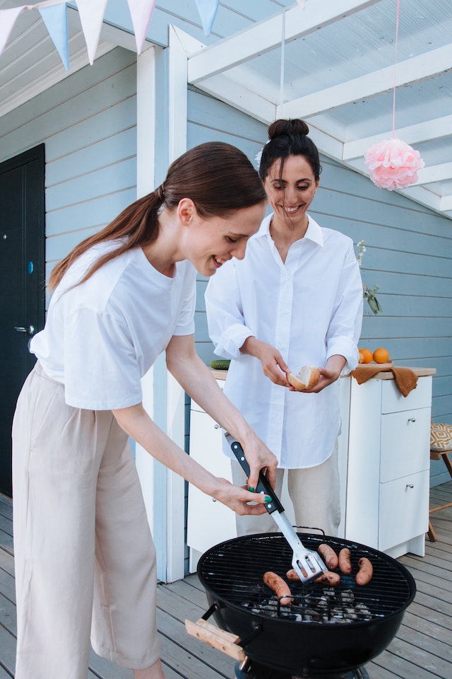 Two women cooking sausages on a grill