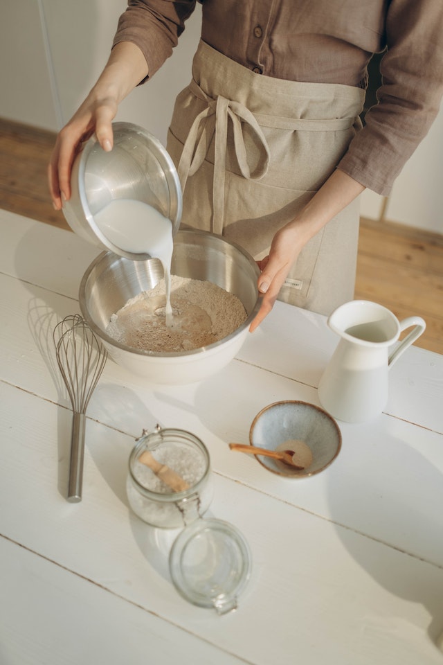 Person adding milk into a mixing bowl with baking ingredients