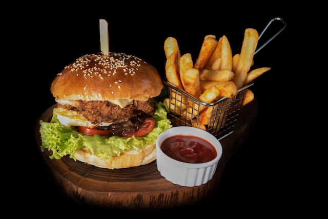 A piece of burger served on a wooden board with ketchup and fries on the side