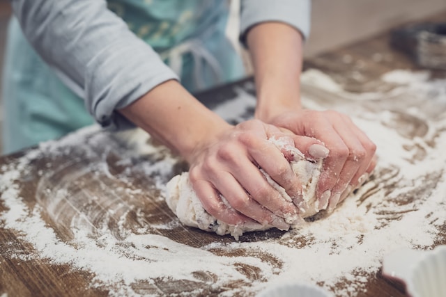 Hands kneading dough on a floured, wooden surface