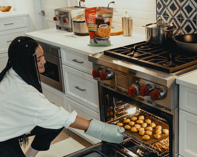 Young woman taking a pan of cookies out of the oven.
