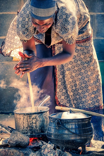 Woman stirs the pot with a wooden stick while cooking in an open fire