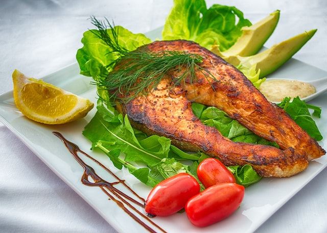 Grilled fish served with tomatoes, avocado slices, a wedge of lemon and some greens