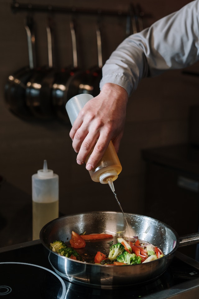 Person drizzling oil on skillet with veggies