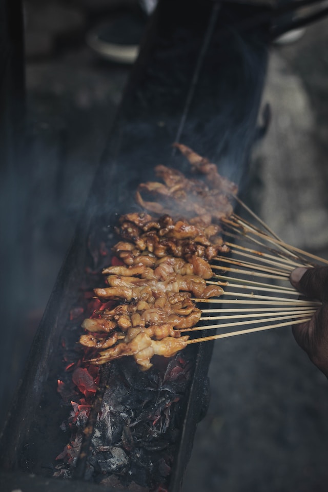 Hand holding skewered meat over a grill