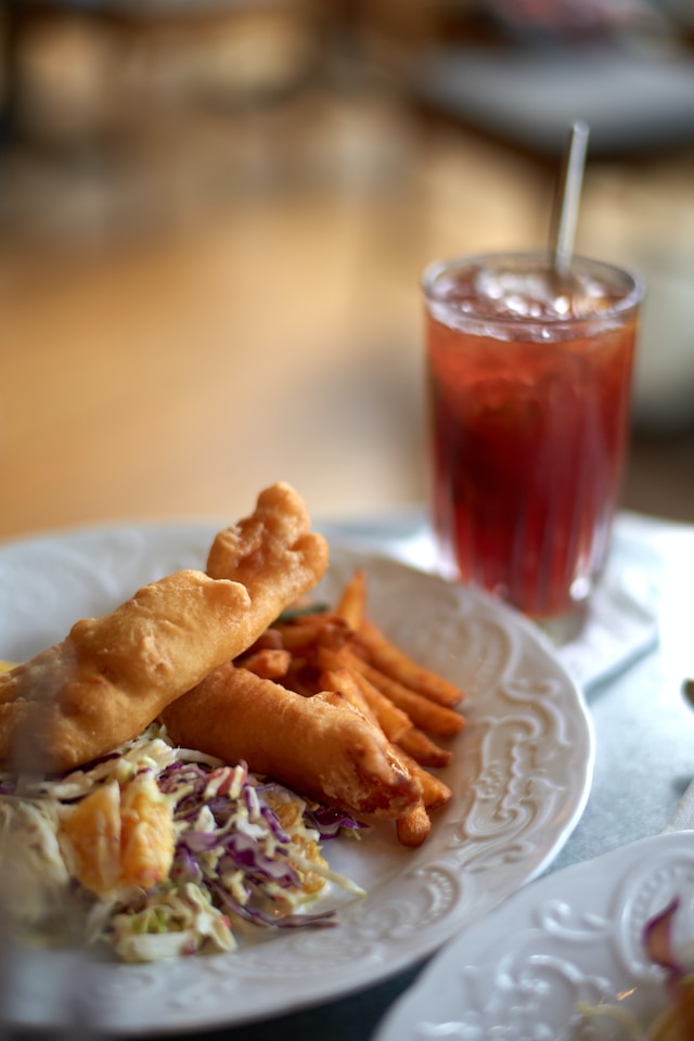 Fish and chips in a white ceramic plate served with a glass of tea