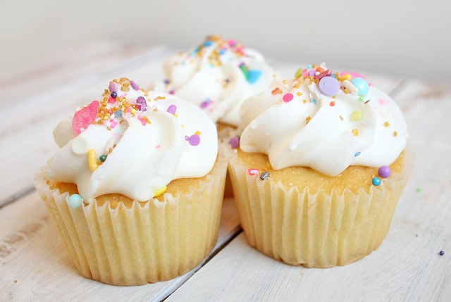 Three vanilla cupcakes with frosting and sprinkles
