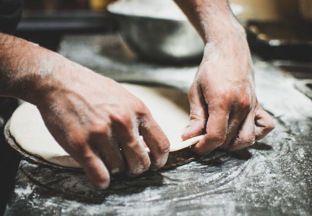 Person shaping a dough on a pizza dish