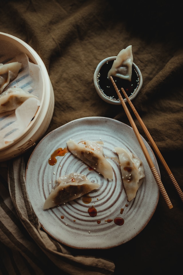 Dumplings in a bamboo steamer and on a ceramic plate served with a soy-sauce dip