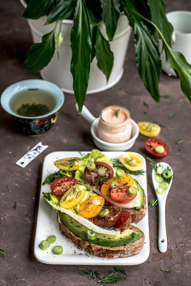 Toast topped with avocado and tomatoes sprinkled with herbs and served with tea