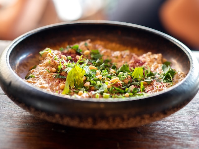 A wooden bowl of hummus topped with grains and chopped herbs