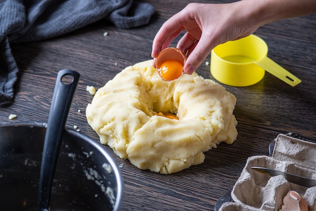 Person adding an egg yolk into a kneaded dough