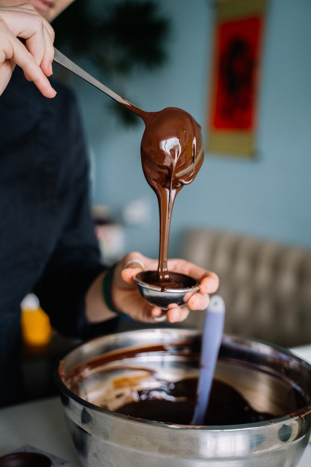 Person scooping melted chocolate into a tiny mold