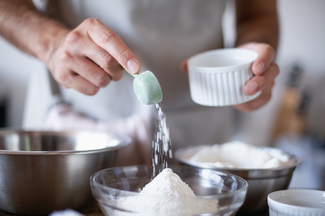 Person scooping ingredients into a mixing bowl