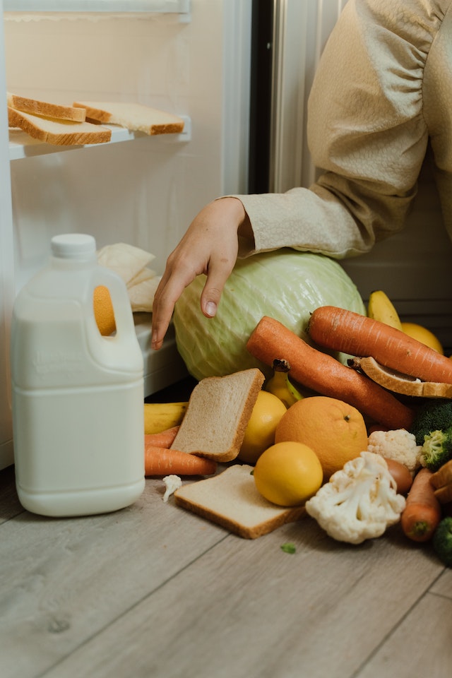 A gallon of milk and a bunch of vegetables beside an open refrigerator