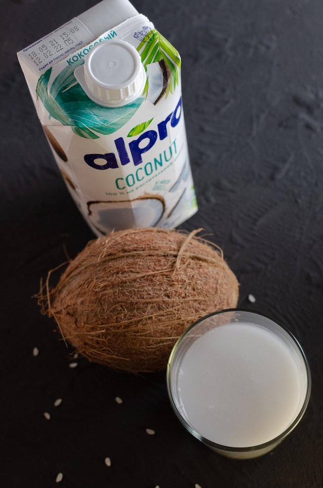 carton of coconut milk with coconut shell and a glass filled with coconut milk